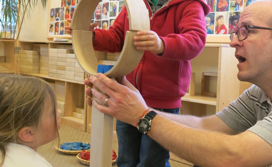 Four-year-olds Jacques and Corinne work with teacher Todd Erickson to balance and secure two semi-circular wooden blocks atop two long, straight ones.