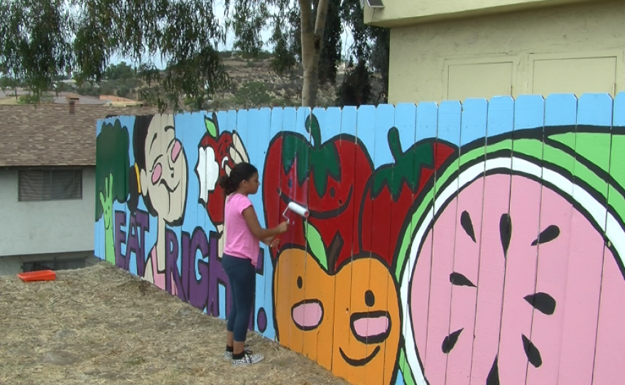 Volunteer Kianna Collins helps cover a new mural near Market Creek Plaza with a coating to protect it from graffiti.