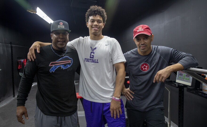 Caleb Williams (C), then a sophomore at Gonzaga College High School, stands with sports performance coach Mark McCain (L) and quarterback trainer Russell Thomas (R) at Athletic Republic in District Heights, Maryland in 2018.