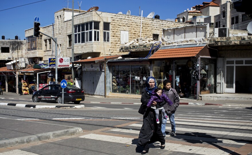 A Palestinian mother and her two children cross the light rail line in East Jerusalem. Nearby is a plaque dedicated to a 16-year-old Palestinian who was kidnapped at the spot and murdered by Israelis in a revenge killing.