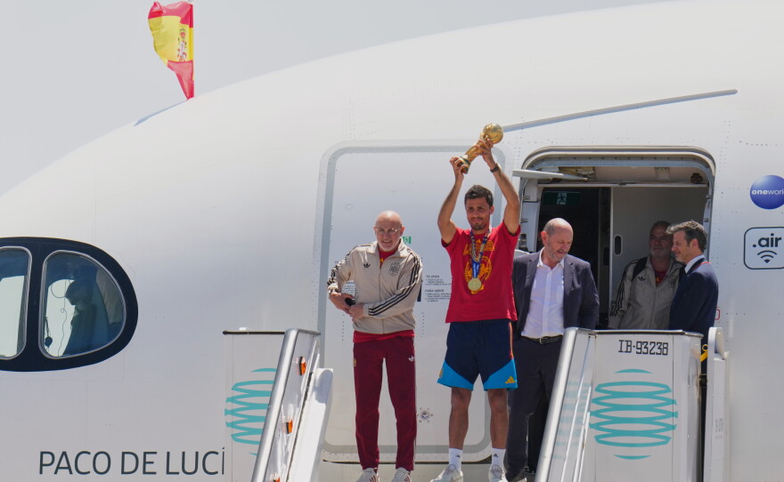 Spain's Rodrigo Hernandez lifts the World Cup trophy alongside Spain head coach Luis de la Fuente, left, and Royal Spanish Football Federation President Rafael Louzan as they arrive at Madrid airport on Monday, July 20, 2026, after Spain defeated Argentina in the World Cup final.