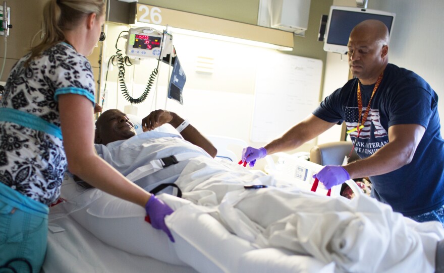 Joleen Beiley and Stephen Gafford lift patient David Eurey using a floating mattress called a HoverMatt, which uses air streams that lift the mattress, making it easy for nursing employees to move a patient from a bed to a gurney.