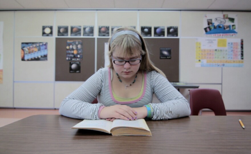 A young girl sits at a desk reading a book as featured in "Is School Enough?" This program examines a new frontier that could reshape education --- the importance of breaking out of the classroom and connecting students into the wider world.