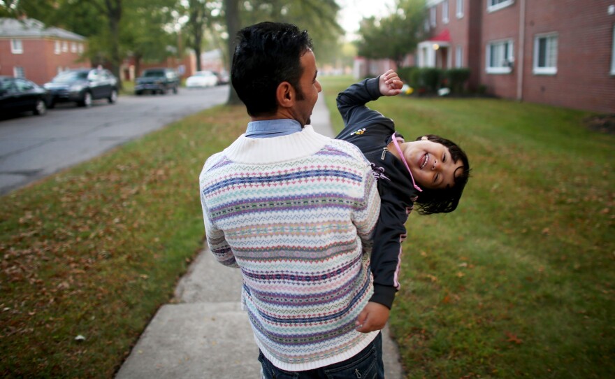 Top: Omar Al-Awad holds his daughter Taiba, 4, as they walk to their home in Toledo, Ohio, where they were recently resettled after fleeing Syria and living in a Jordanian refugee camp for two years. Left: The only possessions Omar brought from Syria were baby photos and his grandmother's identification card. Right: Omar's wife Hiyam watches as the family of five gets ready for school.