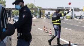 Police officers stop cars at the Melegnano highway barrier entrance, near Milan, Italy, Saturday, April 11, 2020. Using helicopters, drones and stepped-up police checks to make sure Italians don't slip out of their homes for the Easter holiday weekend, Italian authorities are doubling down on their crackdown against violators of the nationwide lockdown decree.