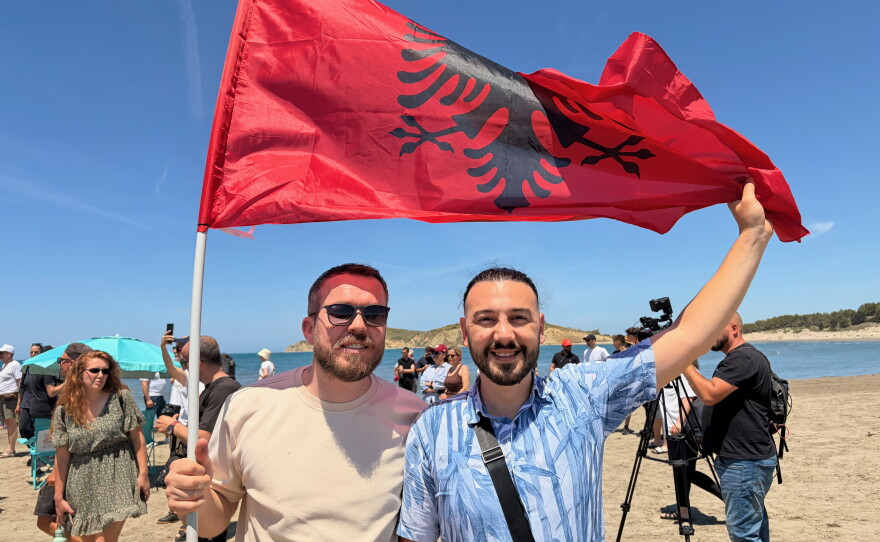 34-year-old Albanian software engineer Albi Batozi, right, holds an Albanian flag with a friend at a protest along the beach in Zvérnec, a place where Batozi says he grew up swimming.