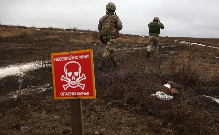 Ukrainian Military Forces servicemen walk past a metal plate which reads "caution mines" on the frontline with Russia-backed separatists.