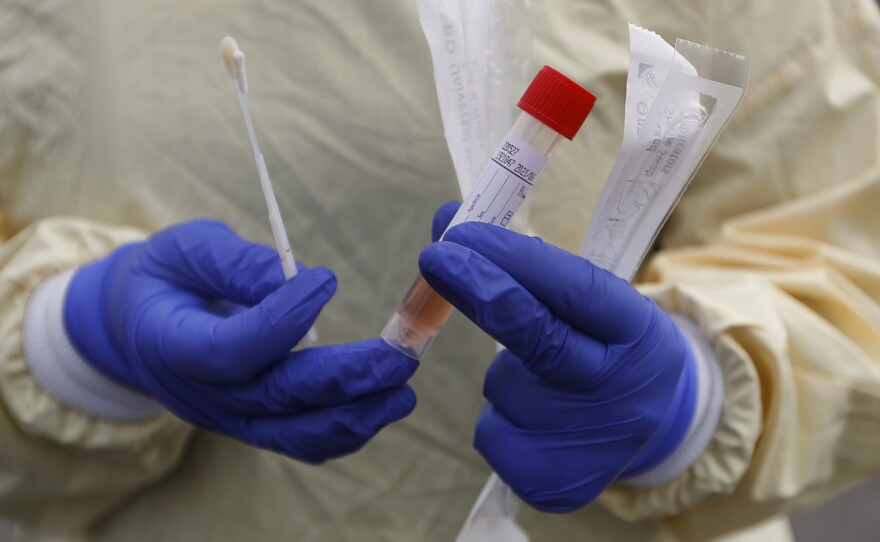 A nurse holds swabs and a test tube to test people for COVID-19 at a drive through station set up in the parking lot of the Beaumont Hospital in Royal Oak, Mich.