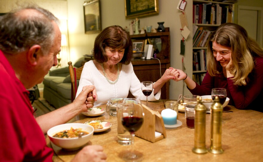 Marianne leads Rick and daughter Laurel, one of the couple's three adult children, in prayer before a meal together.