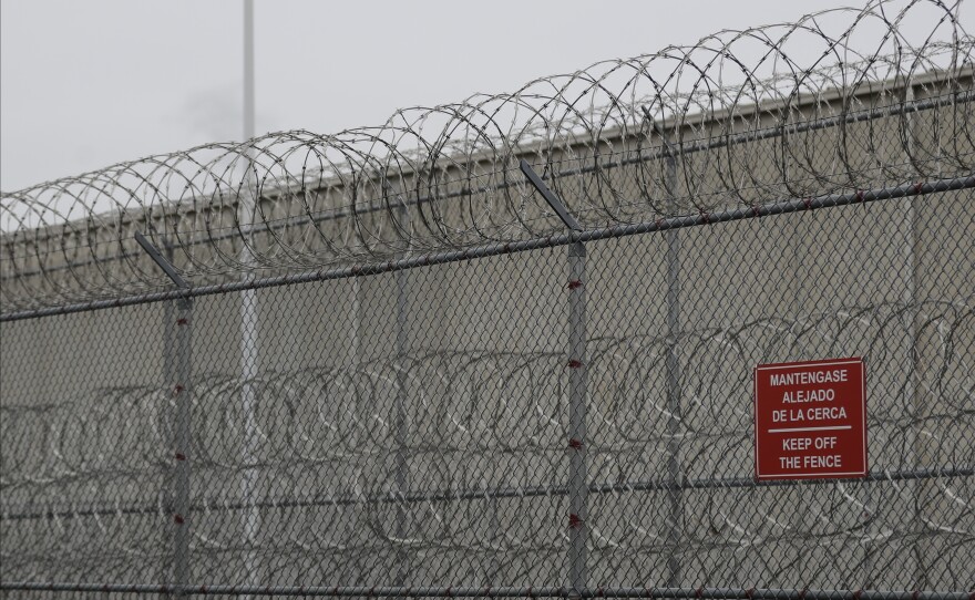 Barbed wire fencing is shown behind a sign in English and Spanish in a recreation yard used by detainees during a media tour of the U.S. Immigration and Customs Enforcement detention center in 2019 in Tacoma, Wash.