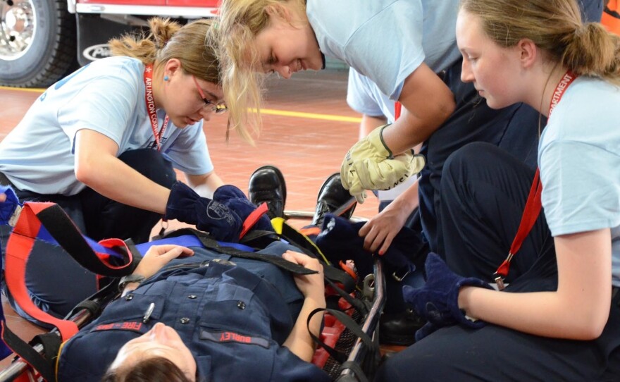 During a drill, teenage girls attending a firefighting camp secure their counselor, firefighter Clare Burley, for a basket rescue at Arlington County's fire station.