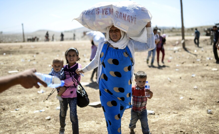 Syrian Kurds carry their belongings after crossing from Syria into Turkey near the southeastern town of Suruc on Saturday. An estimated 130,000 Syrian Kurds have fled fighting and entered Turkey in the past few days.