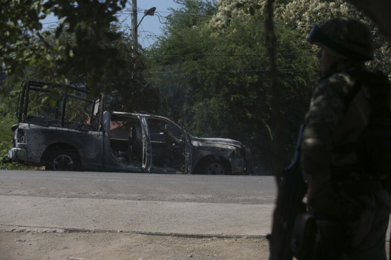 A soldier stands by a charred truck that belongs to Michoacan state police, after it was burned during an attack in El Aguaje, Mexico, Monday, Oct. 14, 2019.