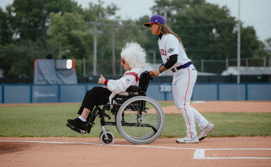 Kelsie Whitmore (right), a pitcher for the San Francisco Firebells and the league's No. 1 draft pick, guides veteran baseball player Maybelle Blair, 99, off the field after the first pitch ceremony on the WPBL's opening day.