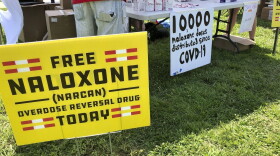 In this file photo, signs are displayed at a tent during a health event in Charleston, W.Va.  Public health officials say the spread of naloxone, also known as Narcan, has dramatically reduced overdose deaths in the U.S.