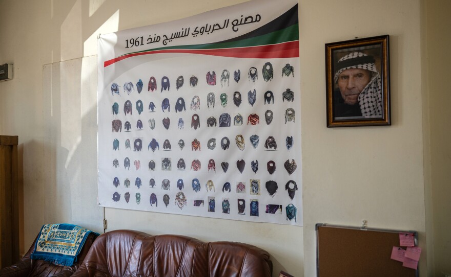 A poster of different keffiyeh designs is displayed beside a portrait of the Hirbawi keffiyeh factory's founder, Yasser Hirbawi.