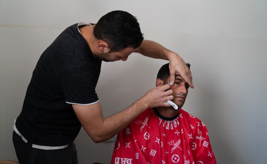 Ibrahim Alfarany gets a shave from a barber at the university. Both are displaced from their homes. With the large number of workers staying at the shelter, they have to sign up on a wait list to get a haircut and shave.