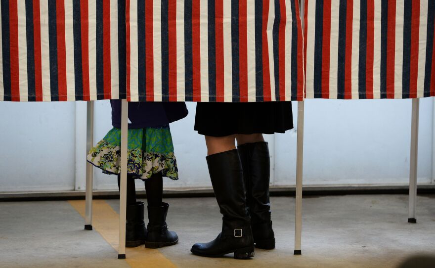 A woman is accompanied by a child inside a voting booth, as she casts her ballot in the New Hampshire presidential primary.