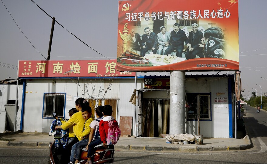 A Uyghur woman rides past a billboard showing China's president, Xi Jinping, joining hands with a group of Uyghur elders at the Unity New Village in Hotan, in the Xinjiang region, in 2018.