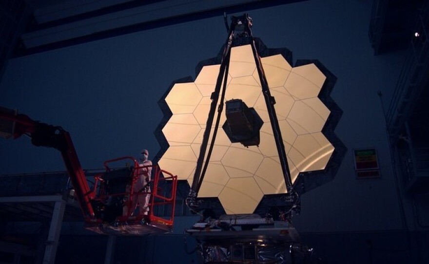 The James Webb Space Telescope's primary mirror is illuminated inside a darkened clean room. The entire telescope is now packed inside a rocket, awaiting launch.