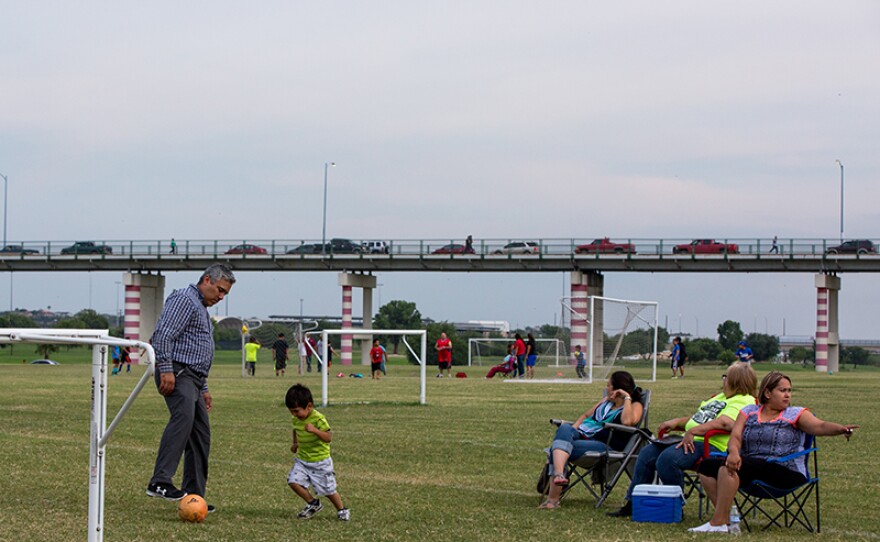 Calai Hernández (third from right) watches her son’s soccer team practice at Shelby Park in Eagle Pass. Behind them is the International Bridge that connects Eagle Pass Texas to Piedras Negras, Coahuila.