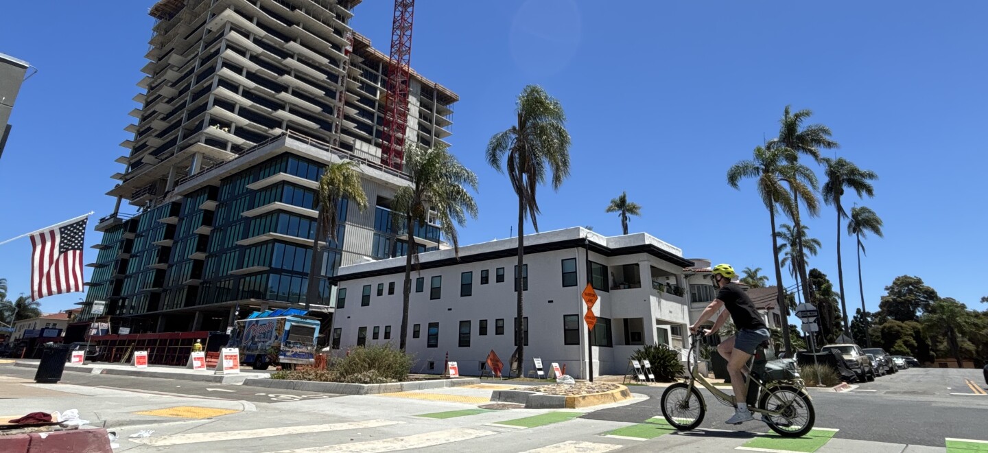 A cyclist rides by the construction site of a high-rise apartment building in Banker's Hill, July 25, 2025.