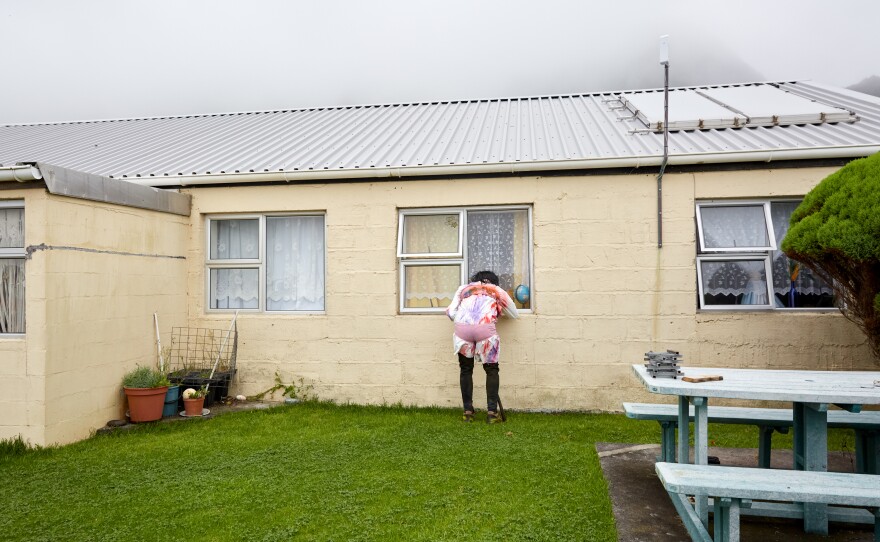 An Okalolie peers through the window of a house, looking for children to frighten. Tristanian women try to outsmart the Okalolies by hiding in groups behind locked doors. Where no "victims" can be found, Okalolies enter the homes of families who have left their doors unlocked.