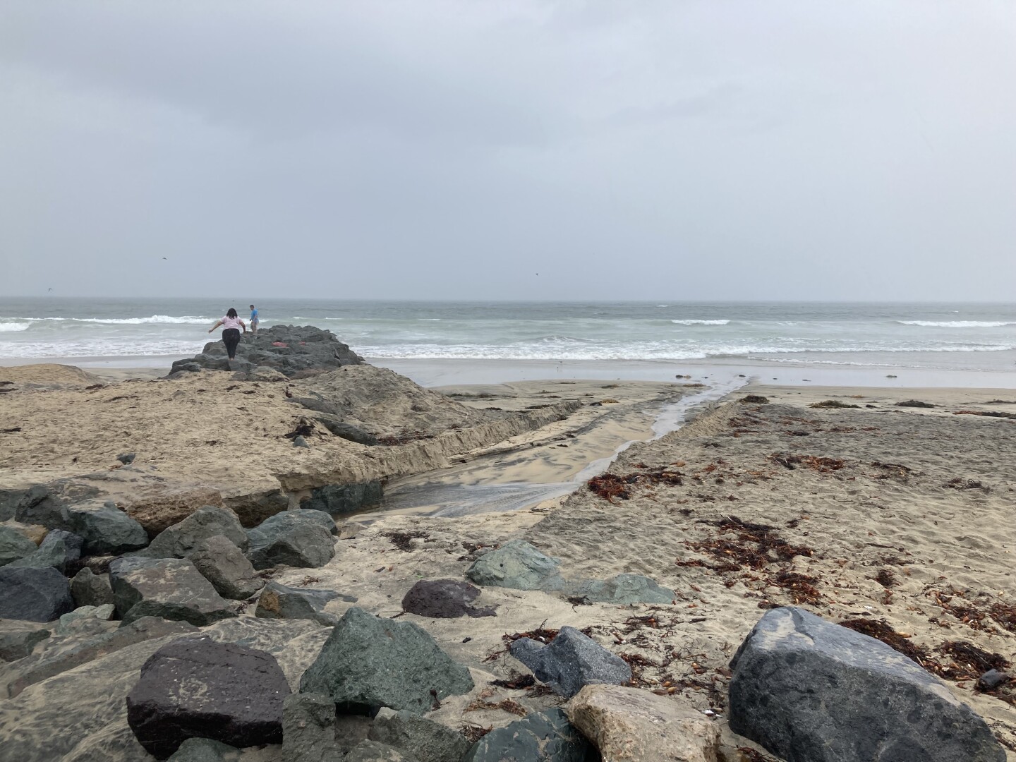 Two people walking on rocks at Imperial Beach near Palm Avenue just before Tropical storm Hilary hits on Aug. 20, 2023