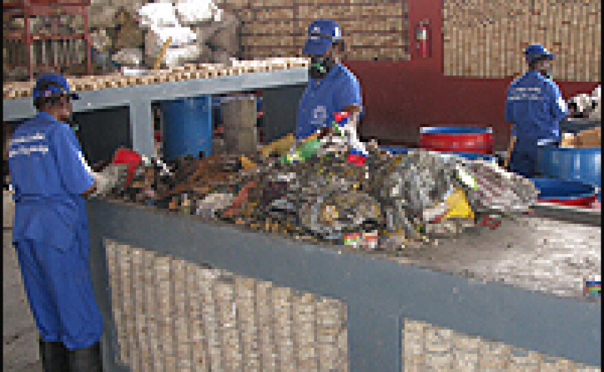 Workers sort garbage at a Port-au-Prince recycling plant. Stacked along the walls and under the table are cakes of recycled paper for cooking fuel.