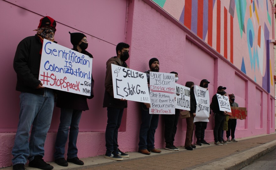 Local organizers protest Bekah Hinojosa's arrest for allegedly spraying graffiti below an Elon Musk-funded mural in downtown Brownsville. The mural, on the side of the Capitol Theater, can be seen behind them.