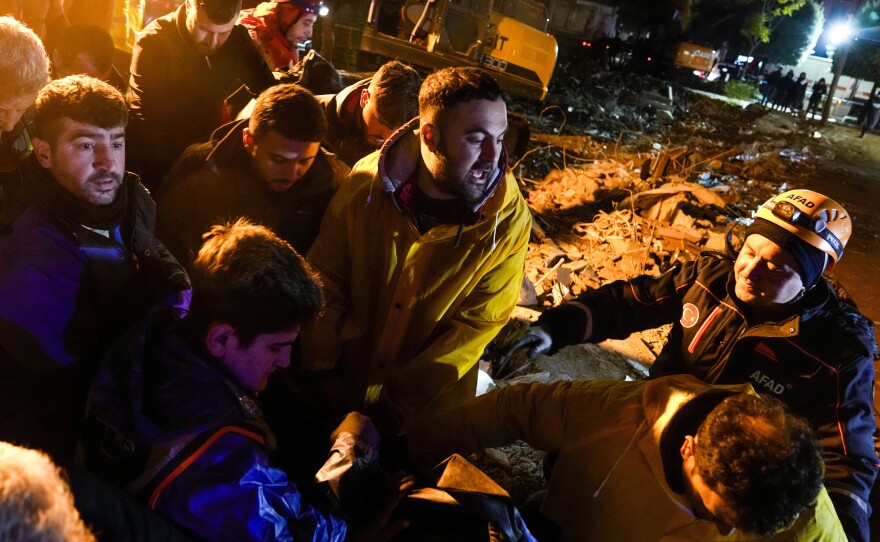 Emergency team members carry the body of a person found in the rubble of a destroyed building in Adana, Turkey, on Monday.