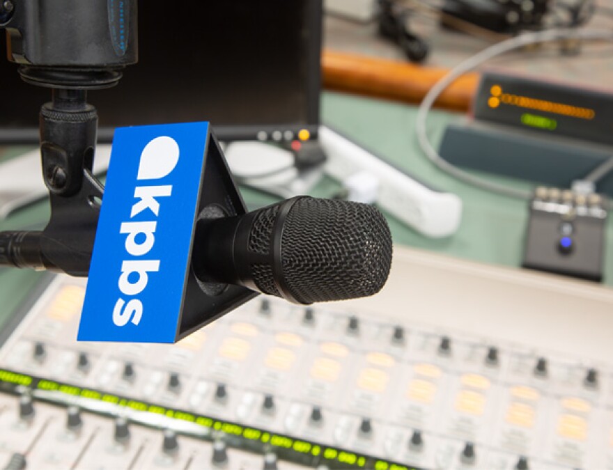 A microphone with a KPBS logo hangs over an audio switchboard in this undated photo.