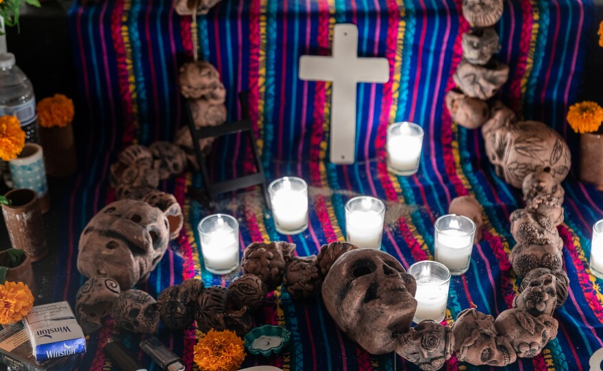 The ofrenda for migrants who died crossing the border features a large Catholic rosary, which are traditionally decorated with prayer beads. This version is is decorated with stylized depictions of human skulls known as calaveras.