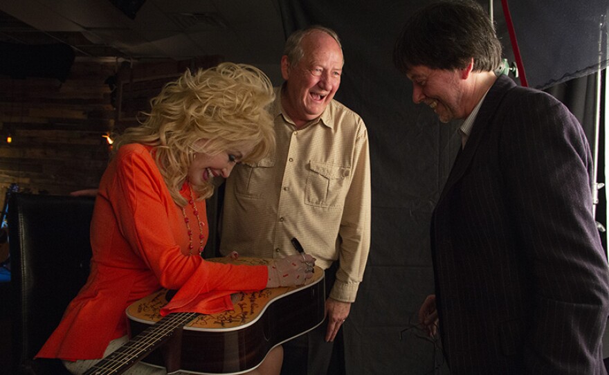 Dolly Parton signs Martin D-28 guitar with Dayton Duncan and Ken Burns to her right. Parton is among the 76 of the 101 country music artists interviewed for the series who signed two Martin D-28 guitars.