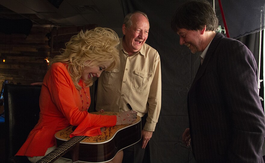 Dolly Parton signs Martin D-28 guitar with Dayton Duncan and Ken Burns to her right. Parton is among the 76 of the 101 country music artists interviewed for the series who signed two Martin D-28 guitars. 