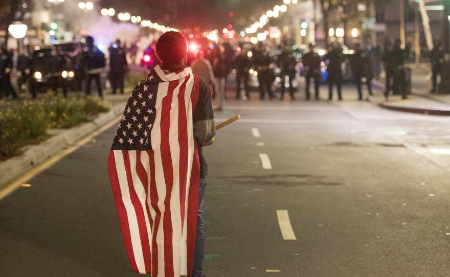 A protester wearing an American flag faces police during an anti-Trump protest in Oakland, California on Wednesday. Thousands of protesters rallied across the United States expressing shock and anger over Donald Trump's election, vowing to oppose divisive views they say helped the Republican billionaire win the presidency.