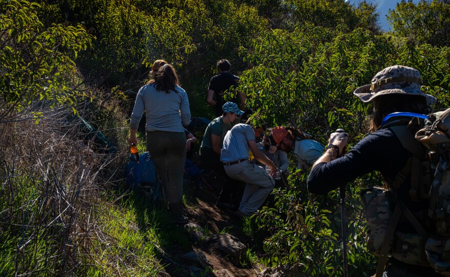 Members of the humanitarian group Borderlands Relief Collective leave non-perishable food and hydration in areas commonly used by migrants walking through rugged terrain on Otay Mountain south of Dulzura, Calif.