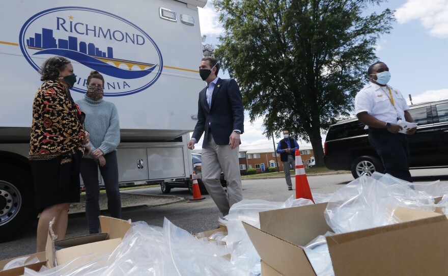 Virginia Gov. Ralph Northam (center) walks past boxes of personal protective equipment that volunteers plan to distribute Tuesday at an event in Richmond. Northam is doing a phased reopening in parts of the state outside the Washington, D.C., suburbs.