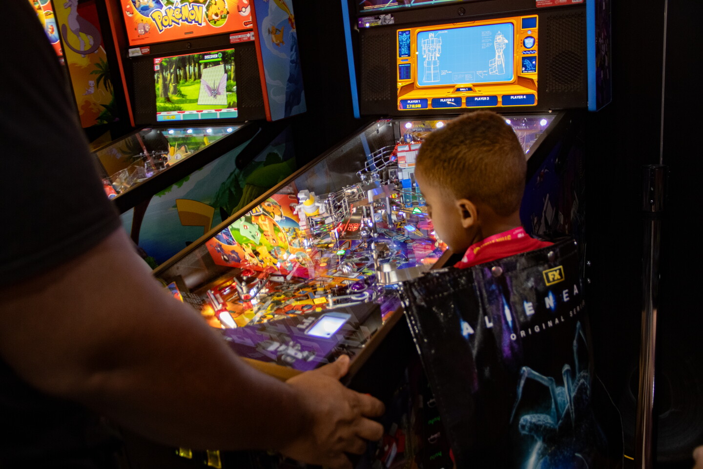 A boy watches his father play a transformer pinball machine at Stern's pop-up at Comic-Con, April 23, 2026.