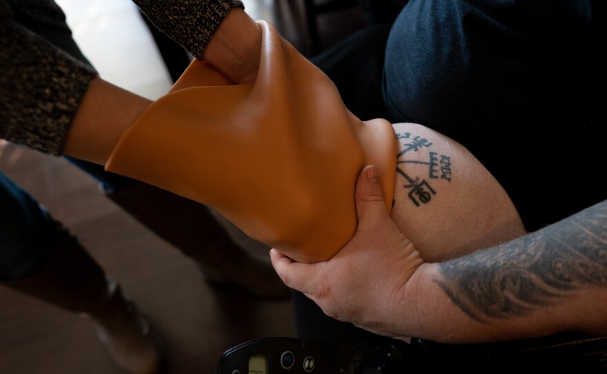 Caretaker Ashlee Williams helps her husband, Former Staff Sgt. J.D. Williams, begin the process of putting on a prosthetic leg.