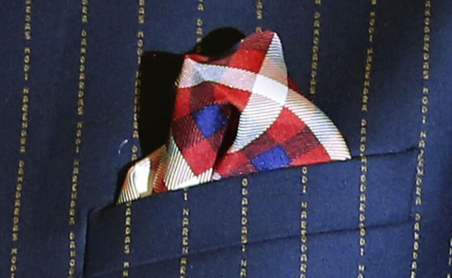 A close-up view of Indian Prime Minister Narenda Modi's dark pinstripe suit, repeatedly embroidered with the words "Narendra Damodardas Modi."