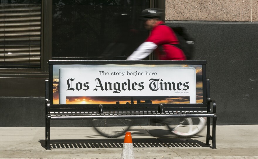 A cyclist rides on the sidewalk past a Los Angeles Times advertisement in downtown Los Angeles. The newspaper is being sued by employees alleging pay discrimination.