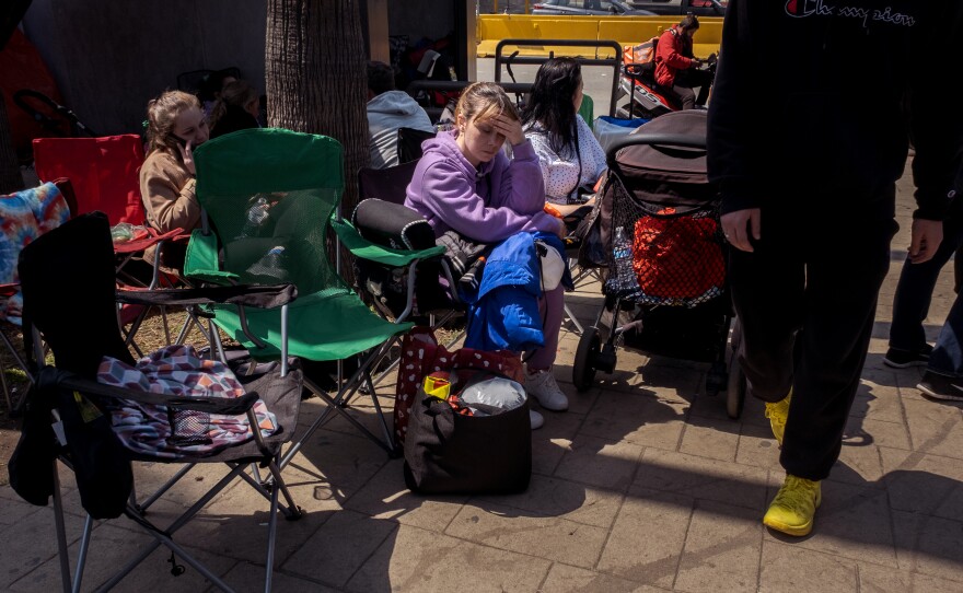 A Ukrainian war refugee woman holds her head, she is tired from the many thousands of miles she's traveled to wait in line at a Tijuana bus stop near the San Ysidro Port of Entry, for her turn to claim alyssum in the United States, April 4, 2022.