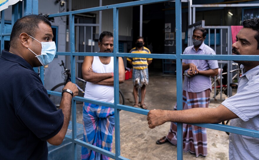 Singapore is seeing a spike in coronavirus cases among its hundreds of thousands of migrant workers. Above, a volunteer from a nonprofit group talks to migrant workers now confined to a factory that was converted to a dormitory as part of the effort to contain the spread of COVID-19.