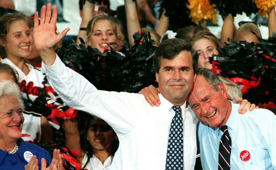 Former U.S. president George Bush embraces his son, Jeb, as Barbara Bush applauds during a rally in downtown Orlando, Florida, October 10, 1994.