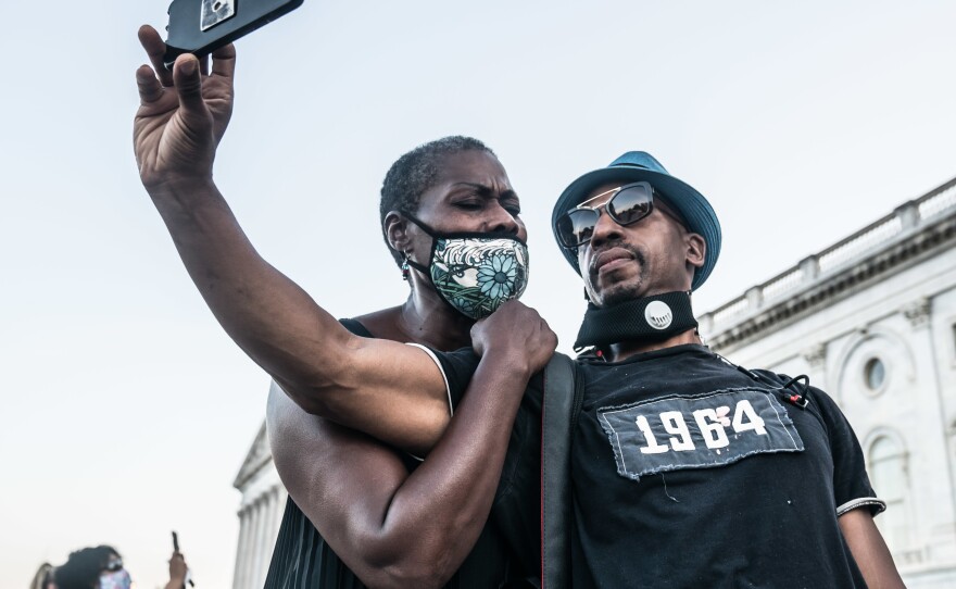 Betty Entzminger, a native Washingtonian, sings as she holds onto designer Kevin Dicksen while they wait in line at the U.S. Capitol to pay respect to John Lewis. Entzminger says what John Lewis means to her is unity and peace — he was a peaceful warrior with a purpose fighting for justice to the end and never ever giving up.