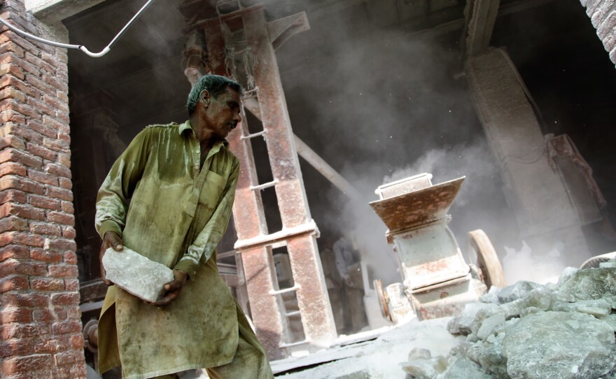 A worker hurls and shovels pink rock salt into a large grinder at a processing plant in Khewra.