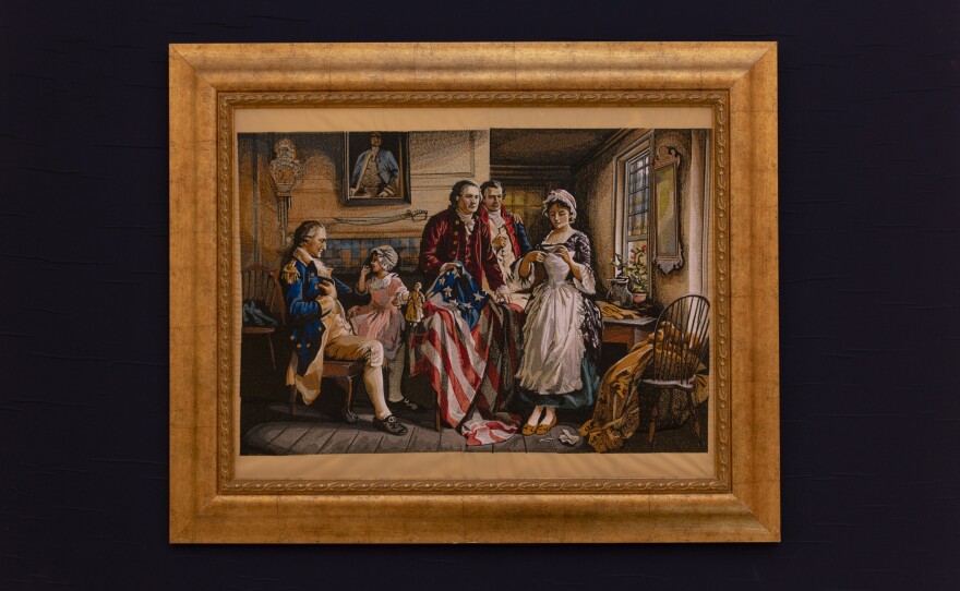 A framed machine-embroidered tapestry depicting historical flag embroidery is on display in the room.