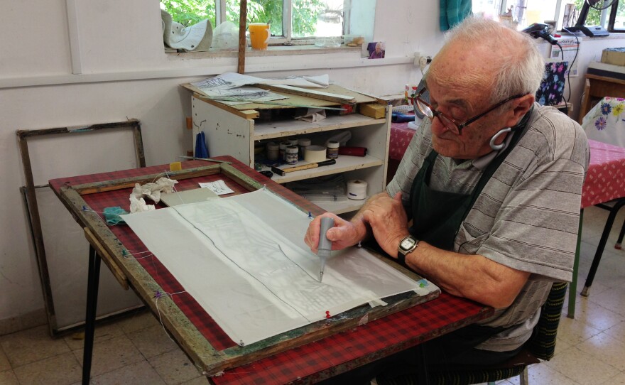The new plan would end a distinction between survivors who arrived in Israel before 1953 and those who arrived after. Mark Taits saw 43 relatives die in the Minsk ghetto during World War II. The 86-year-old moved to Israel from the former Soviet Union in 1991, and hopes to qualify for more assistance under the proposed plan. Here, he paints on silk at the Lifeline workshop.