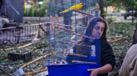 A woman carries a cage with a parrot as she leaves her damaged house following a Russia missile attack in Kyiv, Ukraine, Sunday, July 19, 2026.